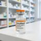 A 10ml NovoRapid vial (insulin aspart) with an orange cap, placed on a clean white pharmacy counter with medical shelves blurred in the background.