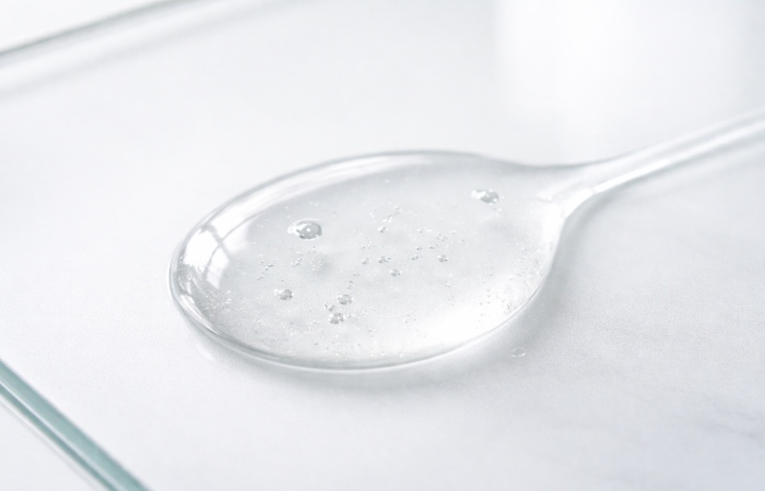 Clear water-based serum drops on glass surface showing thin consistency